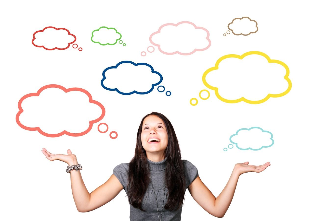 Woman with dark hair looks up at a bunch of colored thought bubbles floating over her head